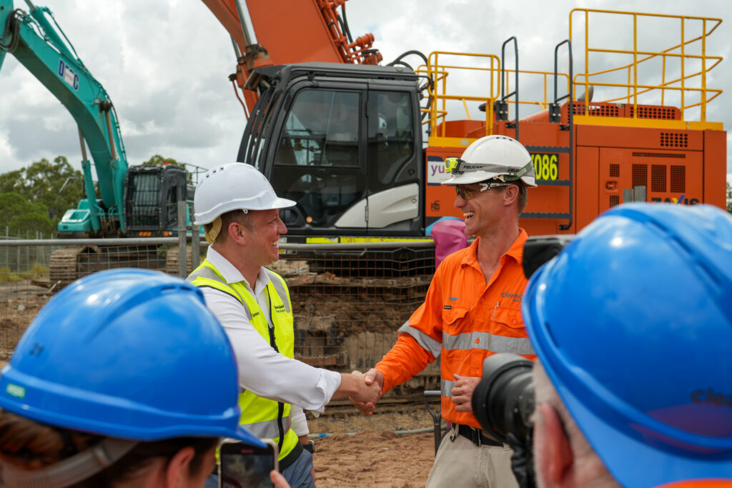 A photo of Queensland Premier Steven Miles shaking hands with a CleanCo worker to celebrate the start of construction of the Swanbank Battery