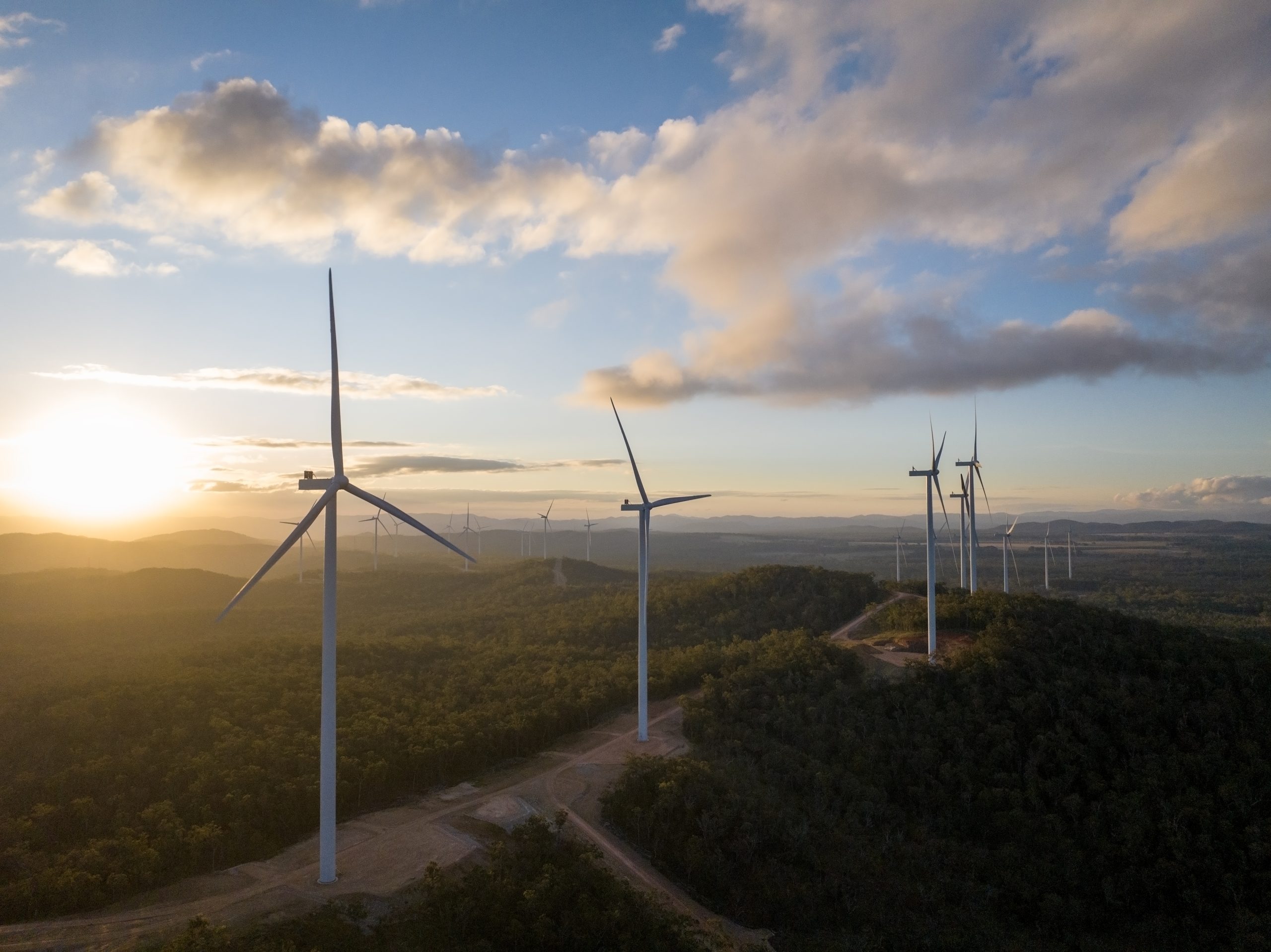 Photograph showing a wind farm at sunset with wind turbines stretching into the distance
