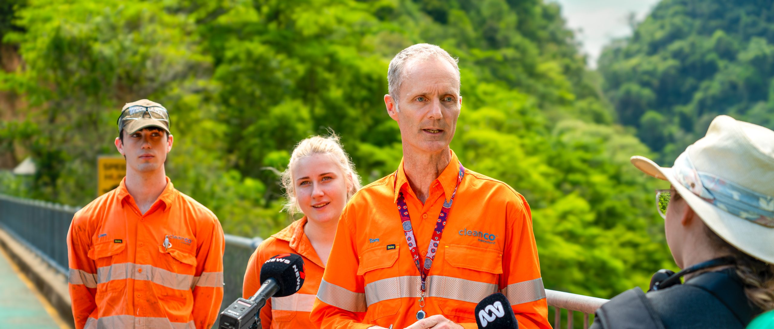 A photograph of CleanCo CEO, Tom Metcalfe speaking at a press conference as two CleanCo workers look on