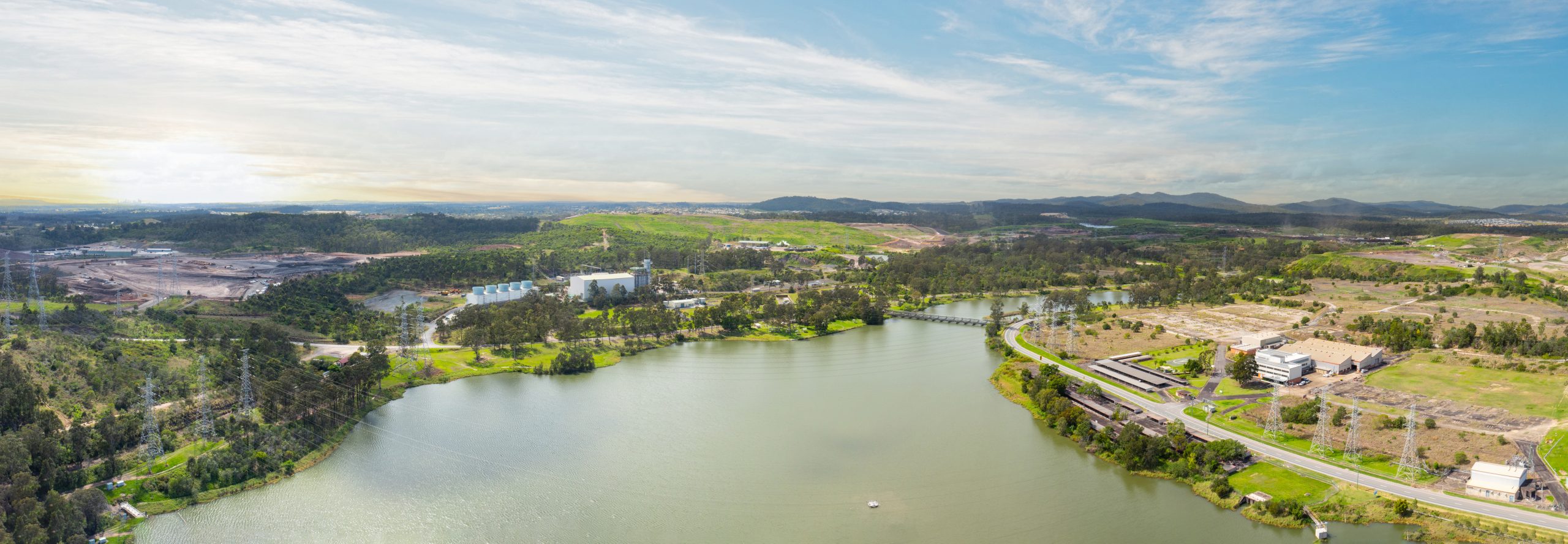 An aerial shot of Swanbank. You can see a large dam surrounded by green hills. You can see the Swanbank Power Station in shot.