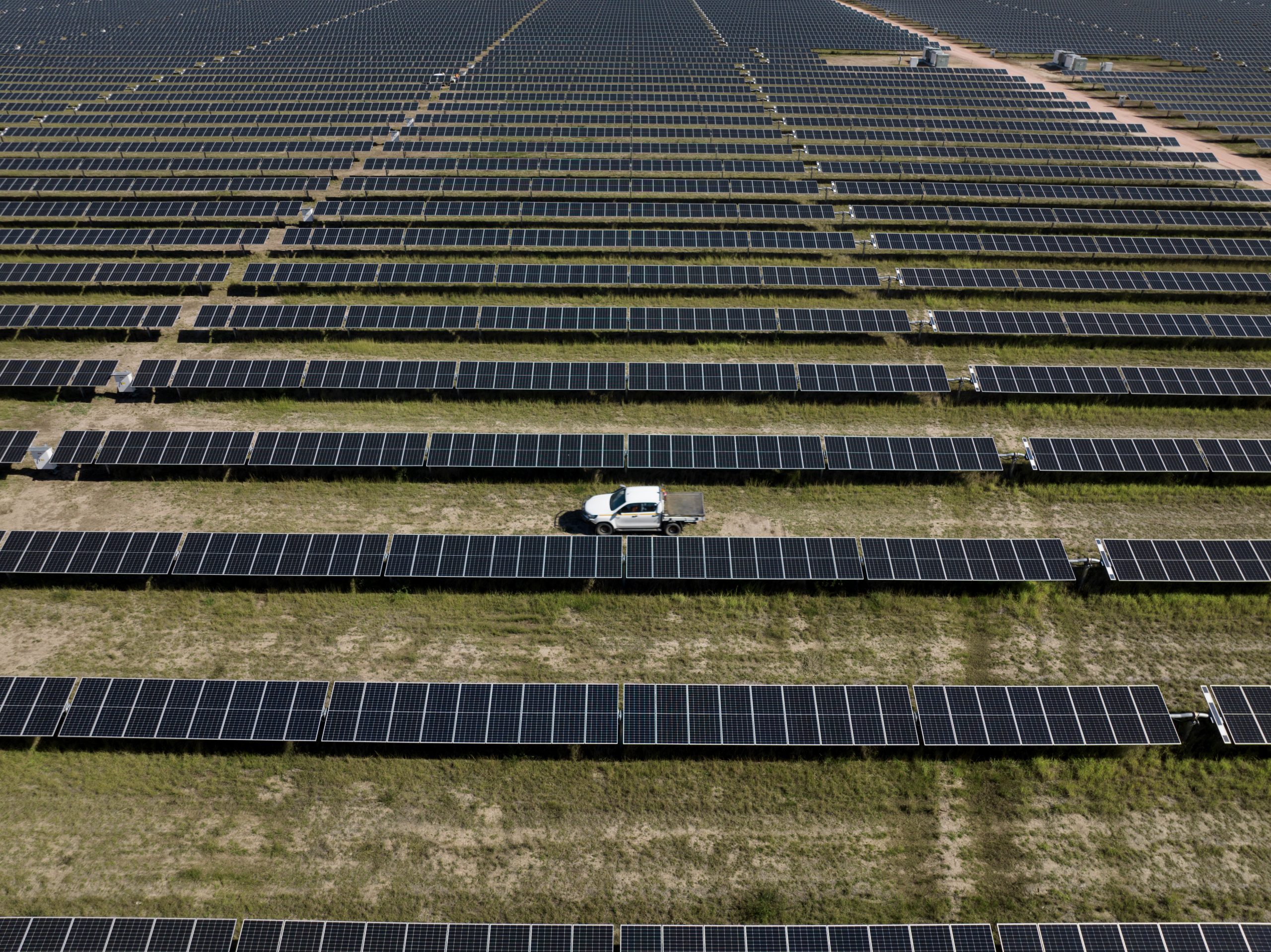 A photograph of a ute driving through a row of solar panels at the Western Downs Green Power Hub
