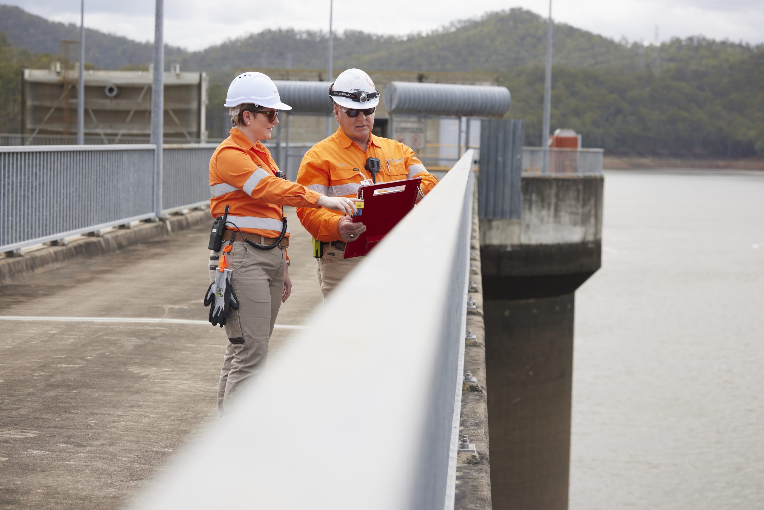 Two Wivenhoe Power Station workers on a bridge looking over the water while they look at a clip board of documents